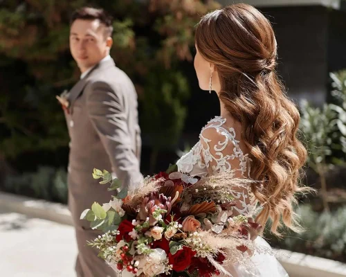 Brautpaar-laeuft-Hand-in-Hand-mit-Anzug-und-Brautkleid-Blumenstrauss-bei-ihrer-Hochzeit